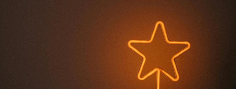 A hand holds a small glowing orange neon star sign against a dark background.